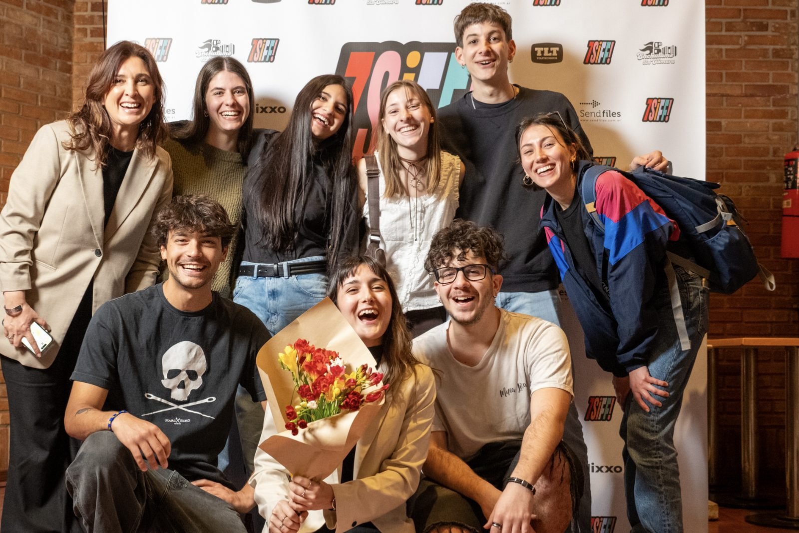 Realizadores y público sonriendo frente al backing del 7SIFF, con un ramo de flores